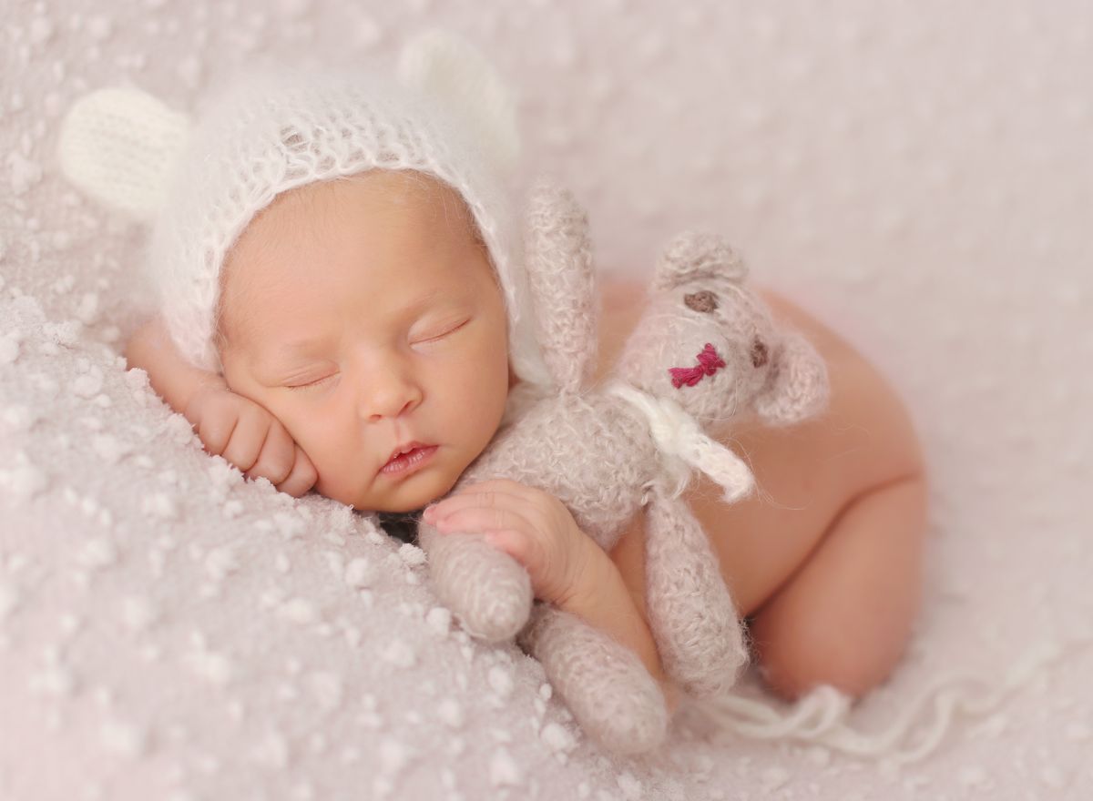 Fotografie spícího novorozeného miminka s čelenkou a s medvídkem v postýlce