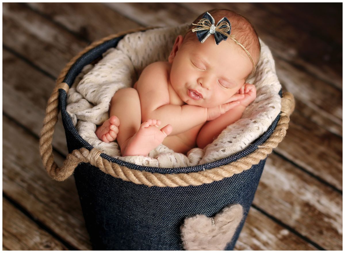 Novorozené miminko vyfotografované spící v modrém textilním kyblíčku s čelenkou a rukama pod hlavou | © Fotoprome.cz
